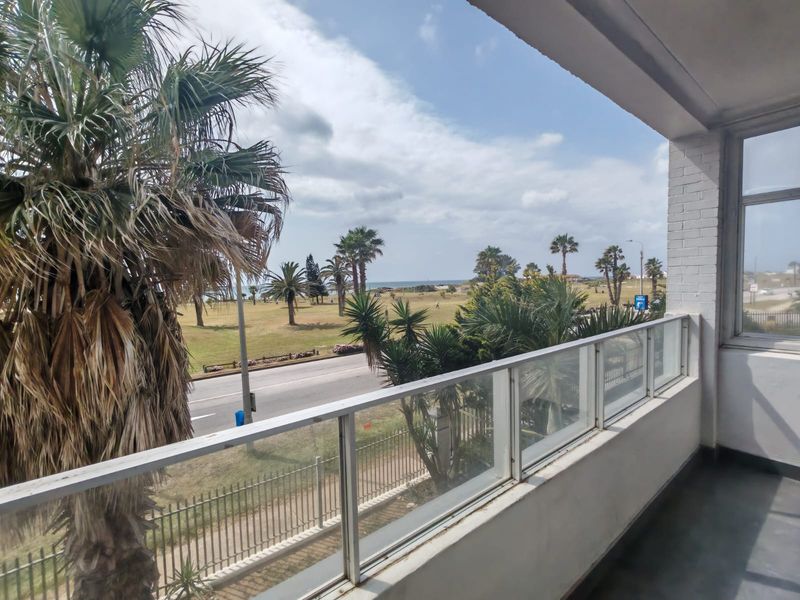 A covered balcony featuring a glass balustrade and painted brick wall, offering an open view of the surrounding parkland and coastal area.
