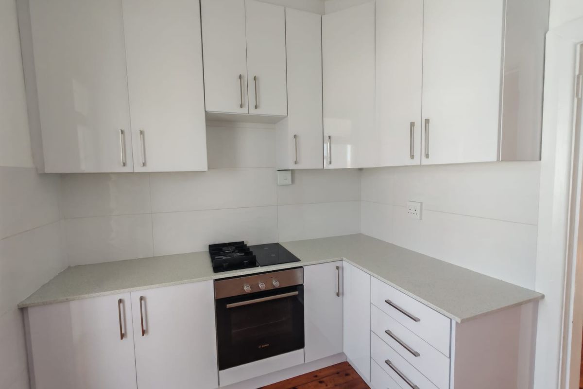 A clean, modern kitchen featuring white cabinetry, stone countertops, a built-in oven, and a gas hob with a tiled splashback.