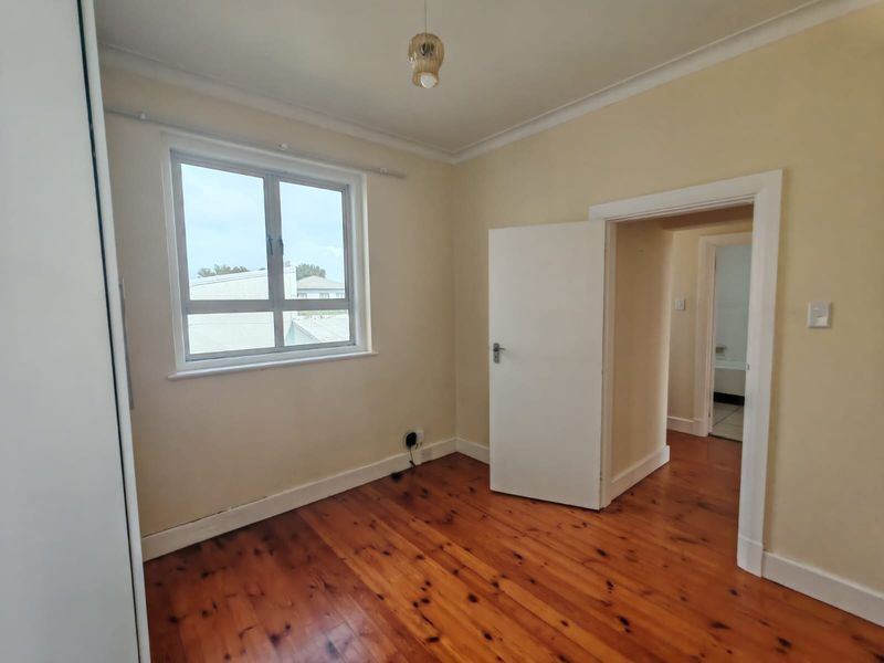 An empty bedroom featuring polished timber flooring, built-in cupboard storage, and neutral wall finishes, with a view into the adjacent hallway and bathroom.