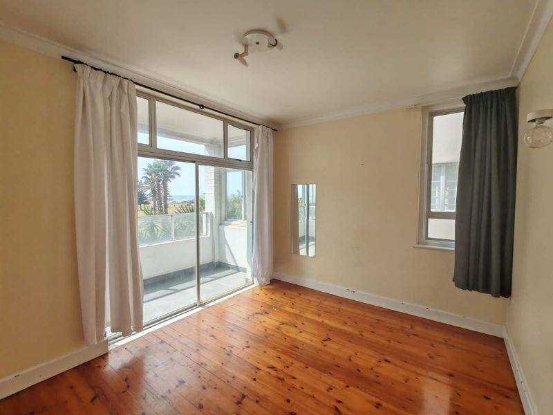 Bright bedroom featuring polished hardwood floors, large sliding glass doors leading to a balcony, and neutral wall tones with natural light.