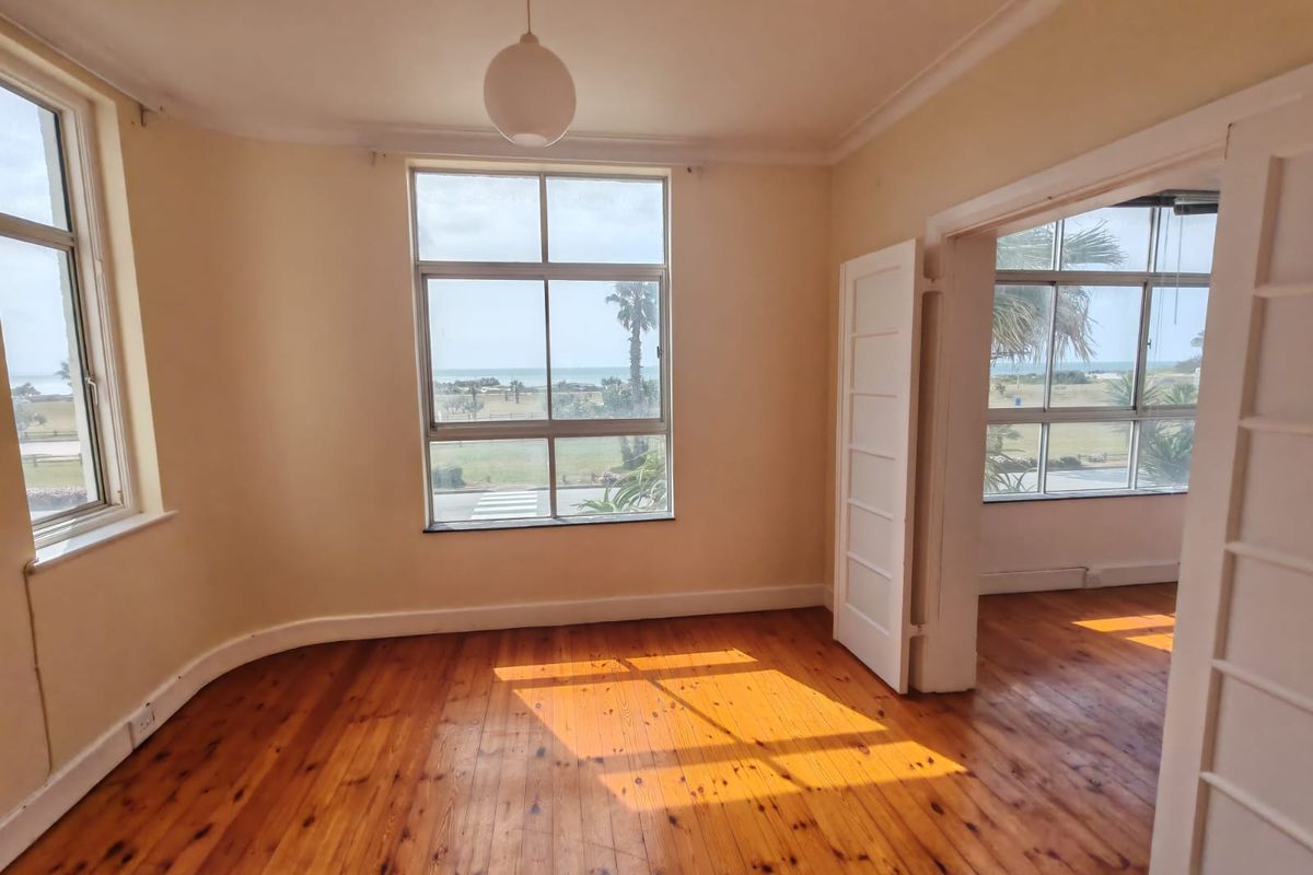 Bright and spacious bedroom featuring original hardwood flooring, large windows with scenic views, and classic coved ceilings in an empty, well-lit space.