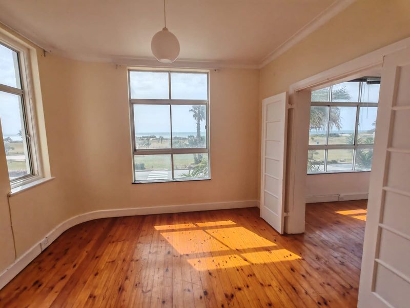 Bright and spacious bedroom featuring original hardwood flooring, large windows with scenic views, and classic coved ceilings in an empty, well-lit space.