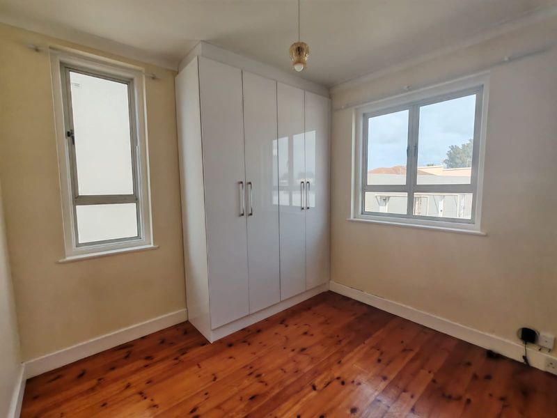 A bright, empty bedroom featuring polished timber flooring, built-in white wardrobes, and dual aspect windows providing natural light.