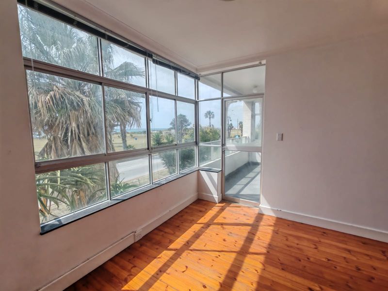 Bright and airy living area featuring polished timber flooring, expansive windows with coastal views, and direct access to an outdoor balcony space.