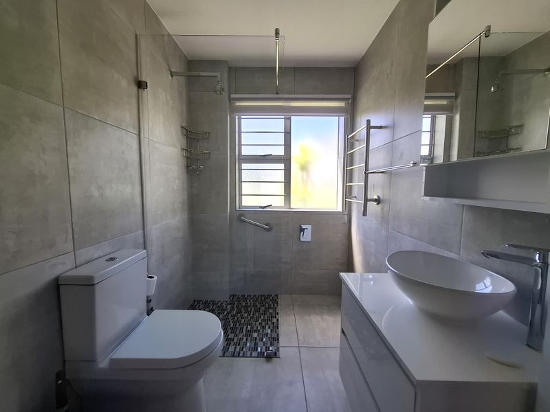 Modern bathroom featuring large format grey wall and floor tiles, a white vanity with vessel sink, and a walk-in shower area.