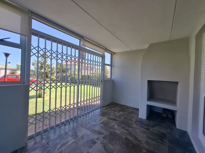 Covered patio area featuring a built-in braai, tiled flooring, and a security gate leading out to the garden.