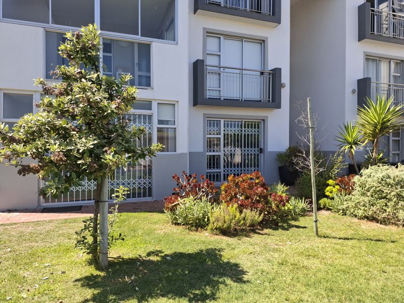 Rear view of the apartment building featuring a landscaped garden, paved walkway, and ground-floor access with security gates and an upper-level balcony.
