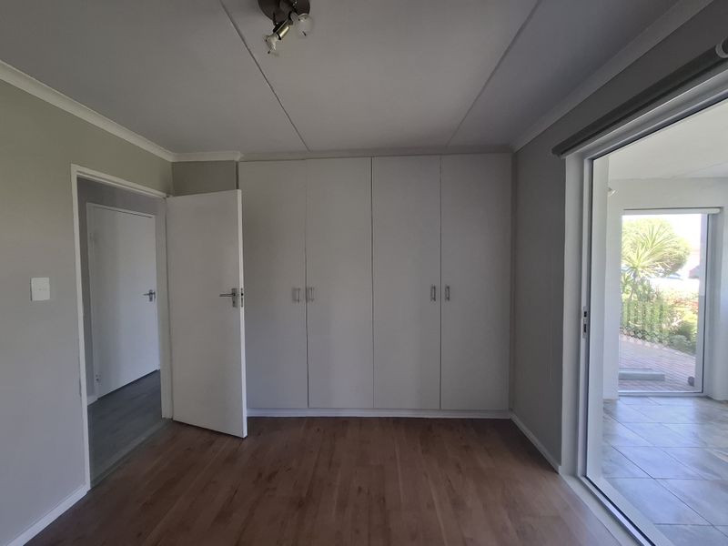 A bright, empty bedroom featuring built-in cupboards, laminate flooring, and a sliding glass door providing access to an outdoor area.