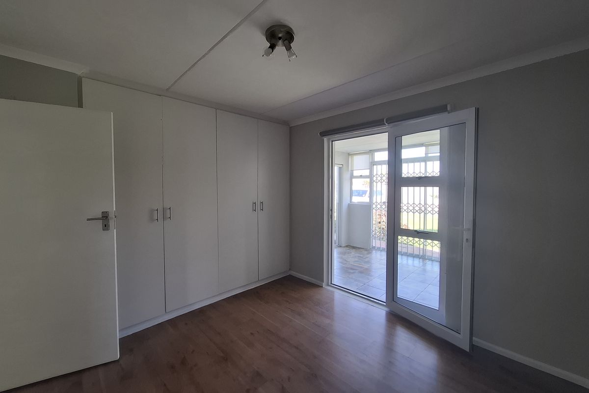 A bright, empty bedroom featuring laminate flooring, ample built-in cupboard storage, and a sliding glass door providing access to an outdoor patio area.