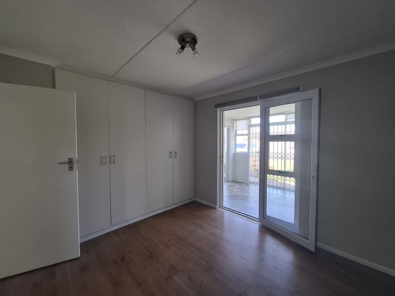 A bright, empty bedroom featuring laminate flooring, ample built-in cupboard storage, and a sliding glass door providing access to an outdoor patio area.