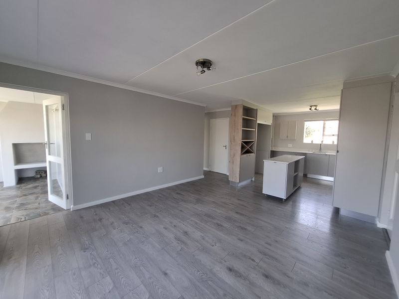 Spacious open-plan living and kitchen area featuring modern laminate flooring, neutral cabinetry, a central island, and an adjacent room with a built-in fireplace.