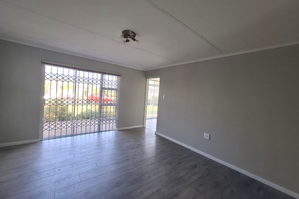 A bright, empty living room featuring modern grey laminate flooring, a sliding glass door with a security gate, and neutral wall finishes.