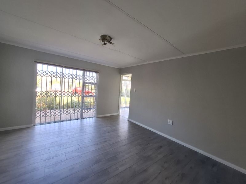 A bright, empty living room featuring modern grey laminate flooring, a sliding glass door with a security gate, and neutral wall finishes.