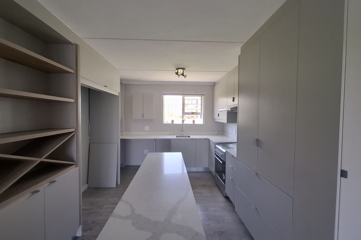 Modern, well-lit kitchen featuring sleek cabinetry, a central stone-topped island, built-in oven, and integrated storage solutions in a clean, contemporary finish.