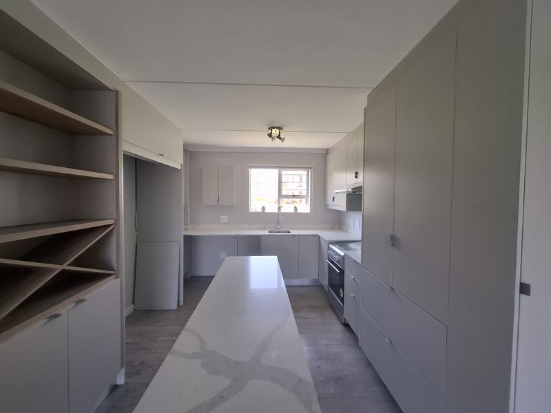 Modern, well-lit kitchen featuring sleek cabinetry, a central stone-topped island, built-in oven, and integrated storage solutions in a clean, contemporary finish.