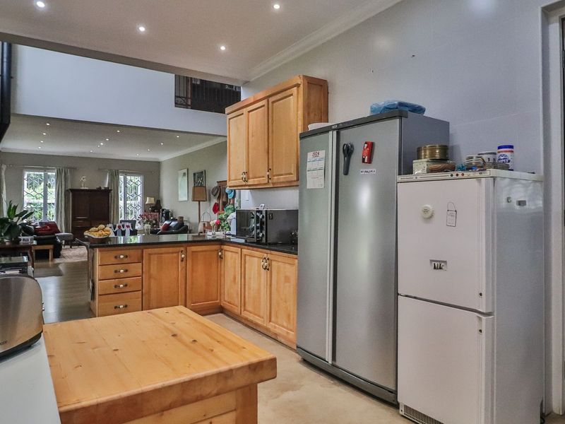 Open-plan kitchen featuring wooden cabinetry and granite countertops, flowing into a spacious living area with double-volume ceilings and recessed lighting.