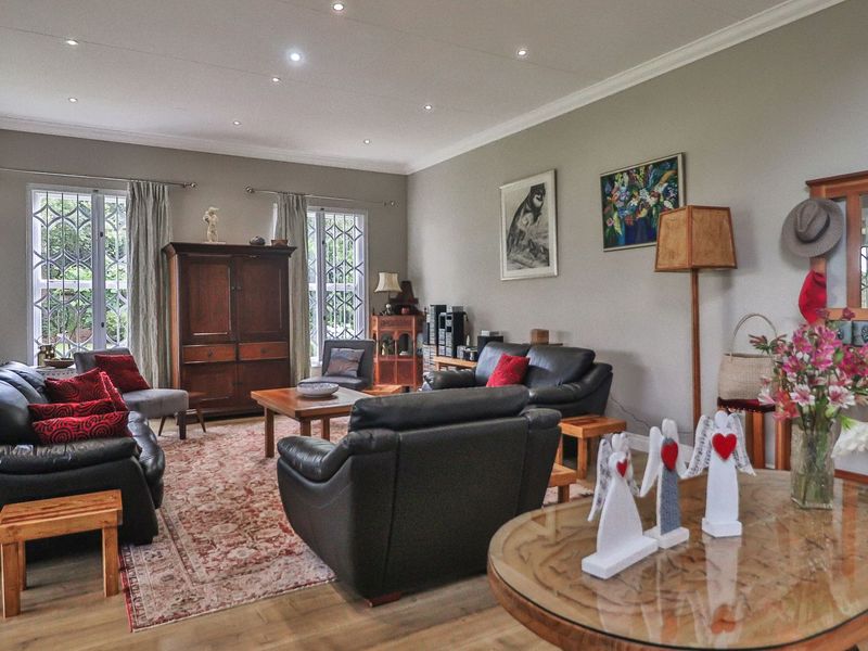 Spacious living room featuring laminate flooring, recessed downlighting, and large windows with security bars, offering a comfortable and well-maintained living space.
