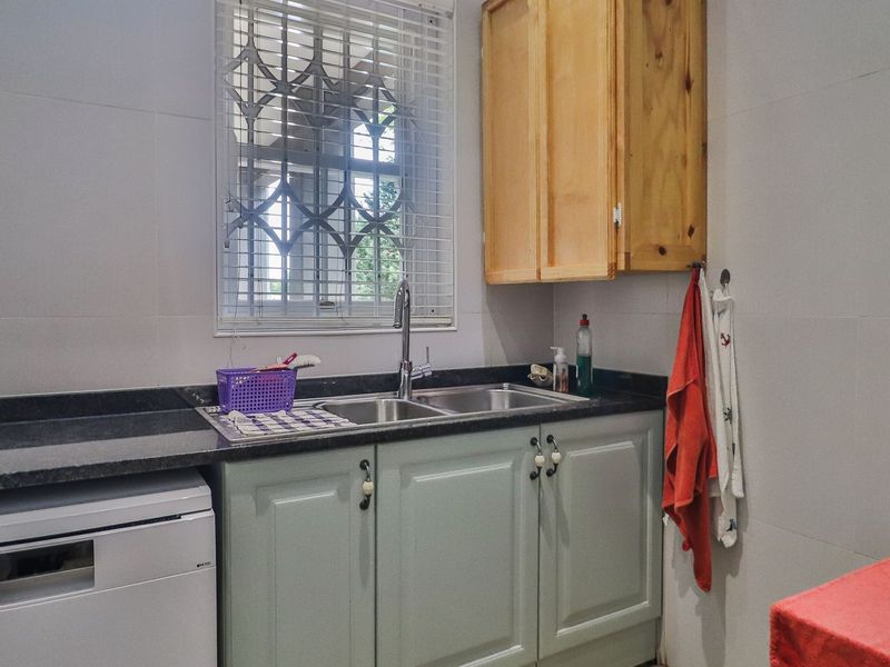 A functional scullery area featuring a double bowl sink, granite countertops, and built-in cabinetry with tiled wall finishes.