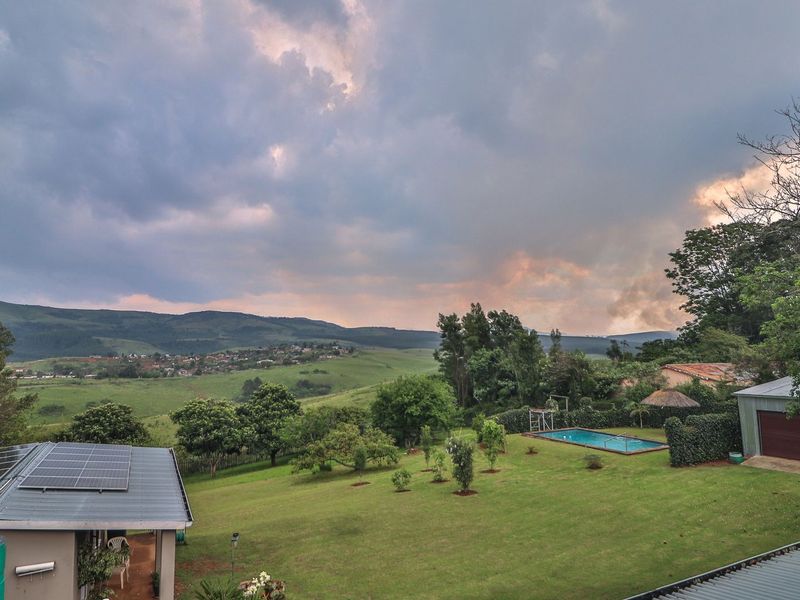 Aerial view of a spacious property featuring a large garden, swimming pool, detached metal garage, and solar panel installation set against a scenic landscape.