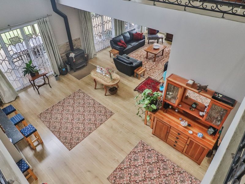 Spacious open-plan living area featuring high ceilings, a wood-burning fireplace, laminate flooring, and a mezzanine level with wrought iron railings.
