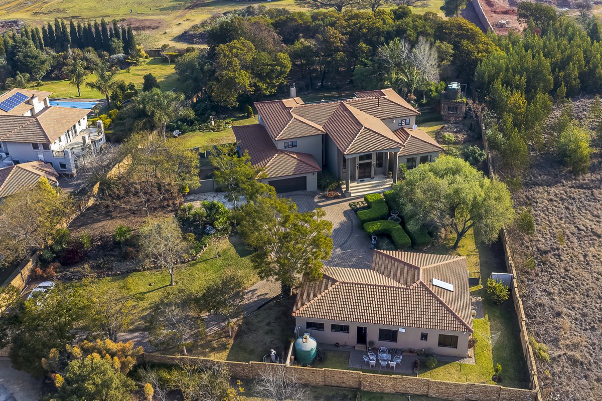 Aerial view of a large residential property featuring multiple buildings, extensive landscaped gardens, paved driveway, and perimeter boundary walls.