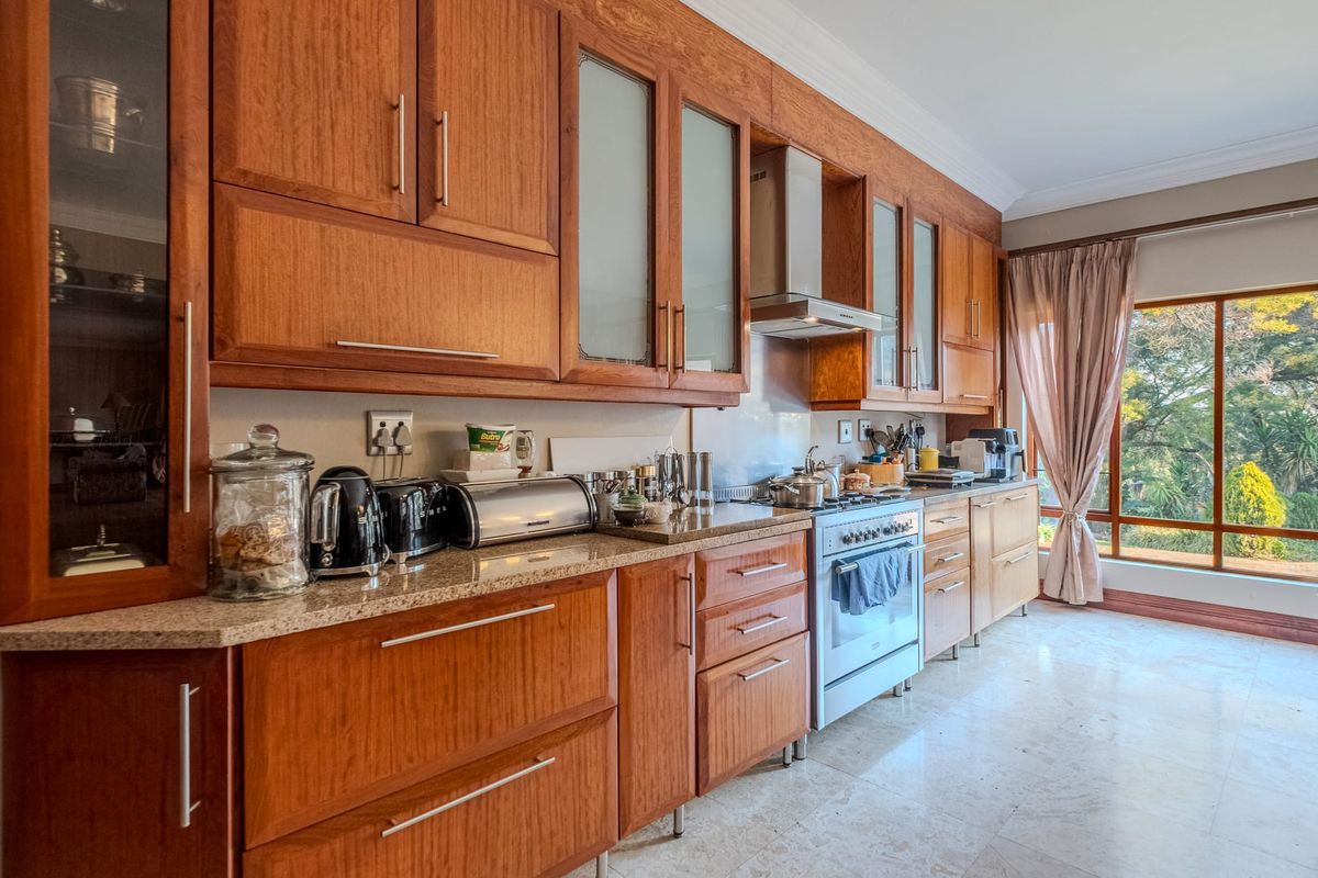 A well-maintained kitchen featuring warm wooden cabinetry, granite countertops, a stainless steel extractor fan, and a freestanding gas stove with large window views.