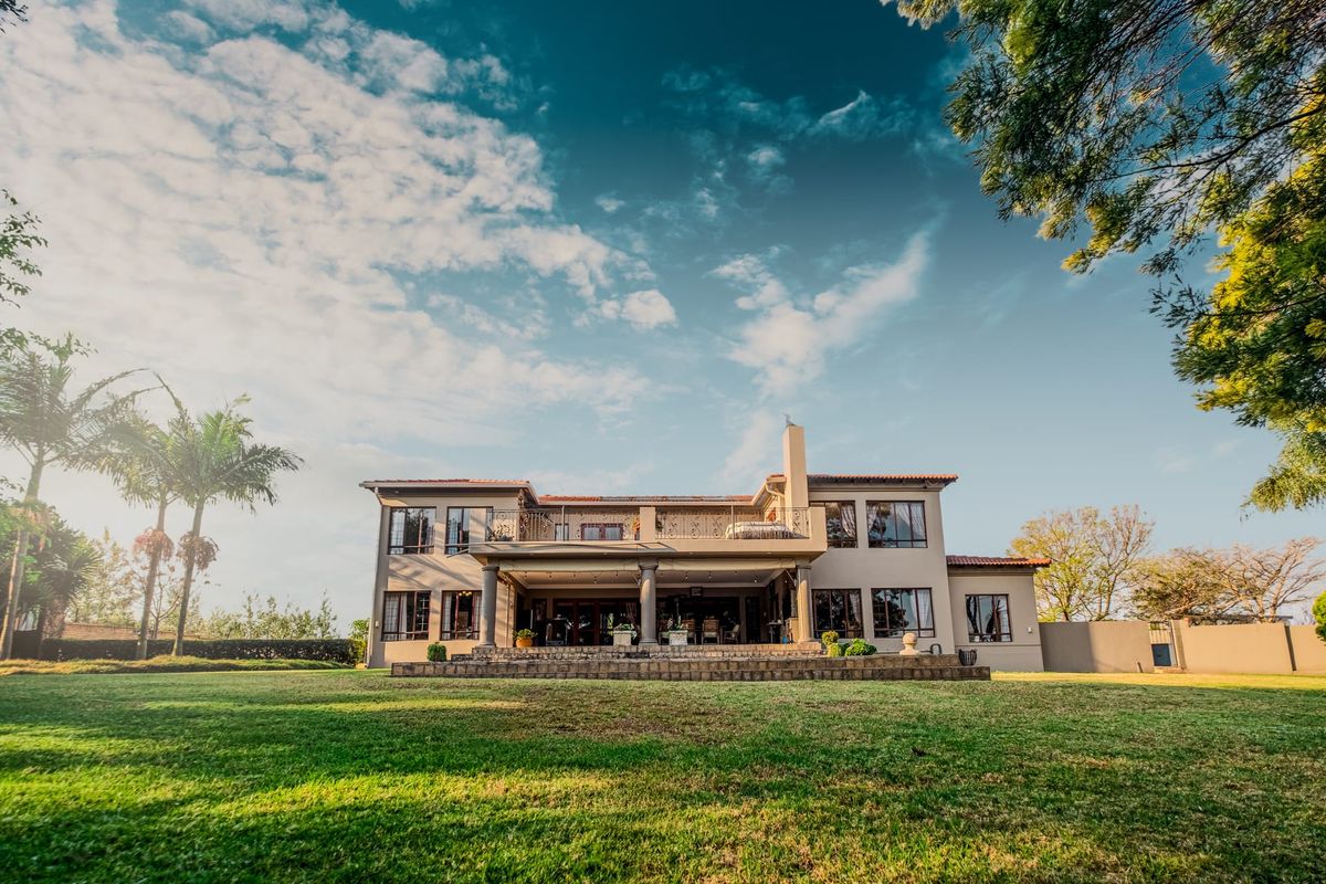 A spacious rear elevation of a two-story house featuring a large lawn, a covered ground-floor patio, and an upper-level balcony.