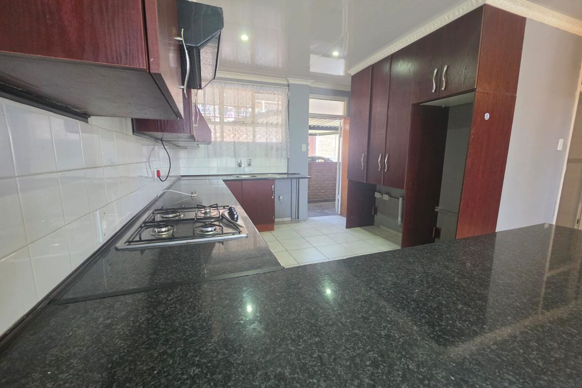 A functional kitchen featuring dark wood cabinetry, granite countertops, a gas hob, and tiled finishes, offering a clean and practical workspace.