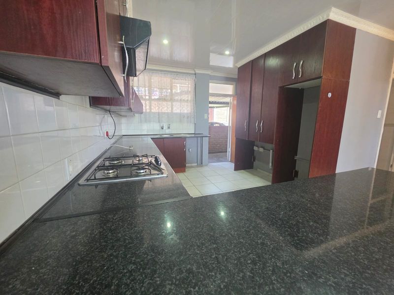 A functional kitchen featuring dark wood cabinetry, granite countertops, a gas hob, and tiled finishes, offering a clean and practical workspace.