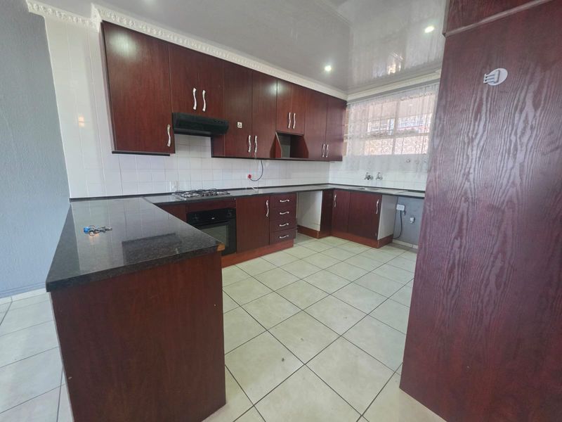 A spacious kitchen featuring dark wood cabinetry, granite countertops, a built-in oven, gas hob, and tiled flooring, offering a functional layout for culinary activities.