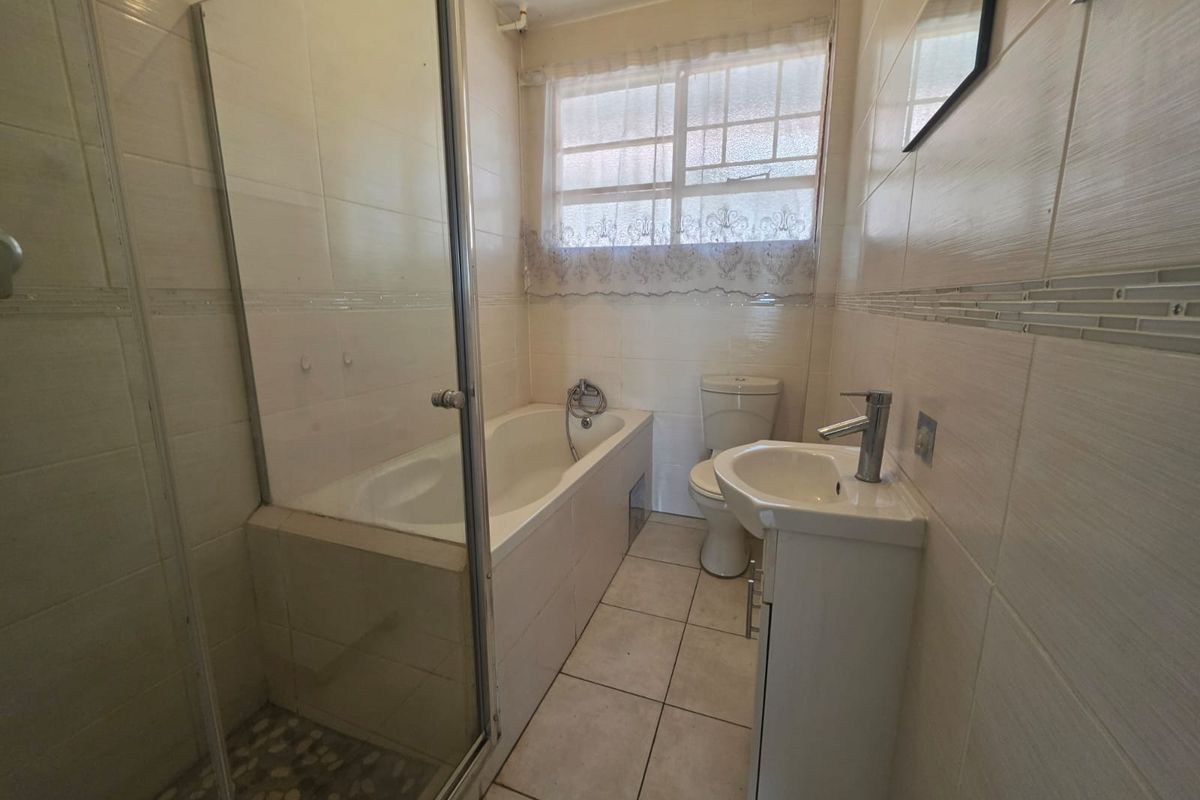 A functional bathroom featuring a built-in bathtub, separate glass shower enclosure, pedestal washbasin, and toilet with neutral tiled finishes.