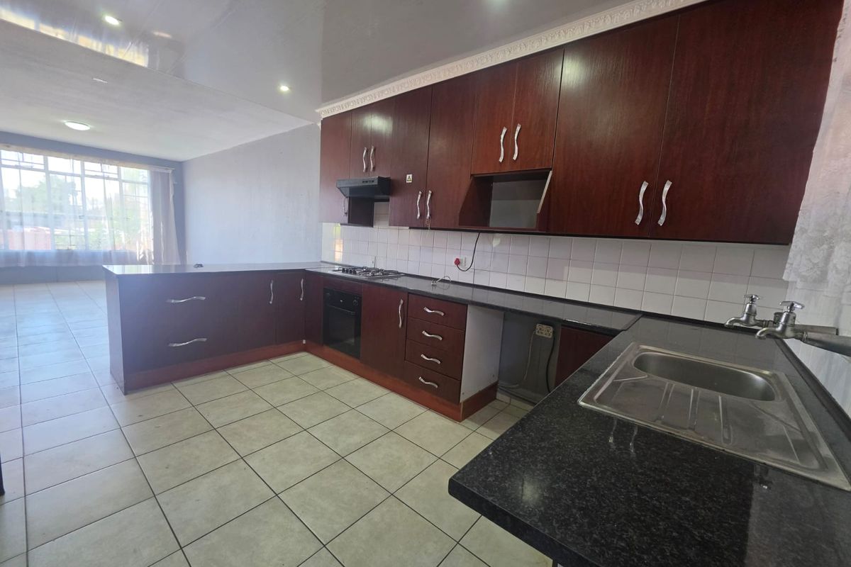 Spacious open-plan kitchen featuring dark wood cabinetry, granite countertops, built-in oven, gas hob, and tiled flooring, offering a functional layout for modern living.