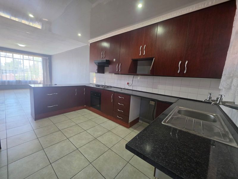 Spacious open-plan kitchen featuring dark wood cabinetry, granite countertops, built-in oven, gas hob, and tiled flooring, offering a functional layout for modern living.