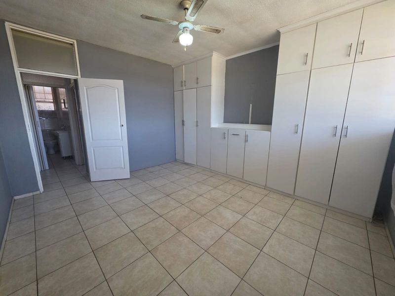 An empty bedroom featuring tiled flooring, built-in cupboards, and a ceiling fan, with direct access to an adjacent bathroom.