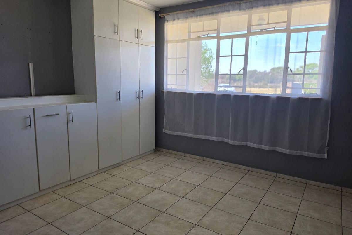A bright, empty bedroom featuring neutral tiled flooring, dark grey walls, and ample built-in cupboard storage space.