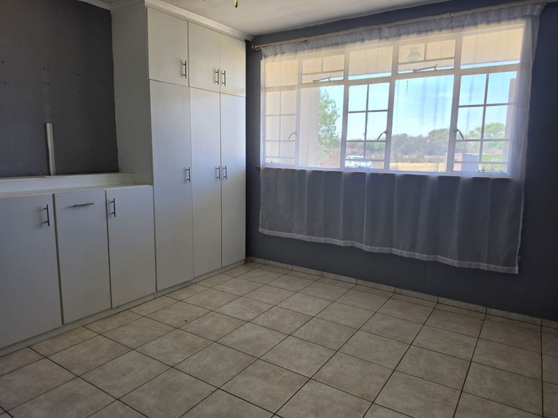 A bright, empty bedroom featuring neutral tiled flooring, dark grey walls, and ample built-in cupboard storage space.