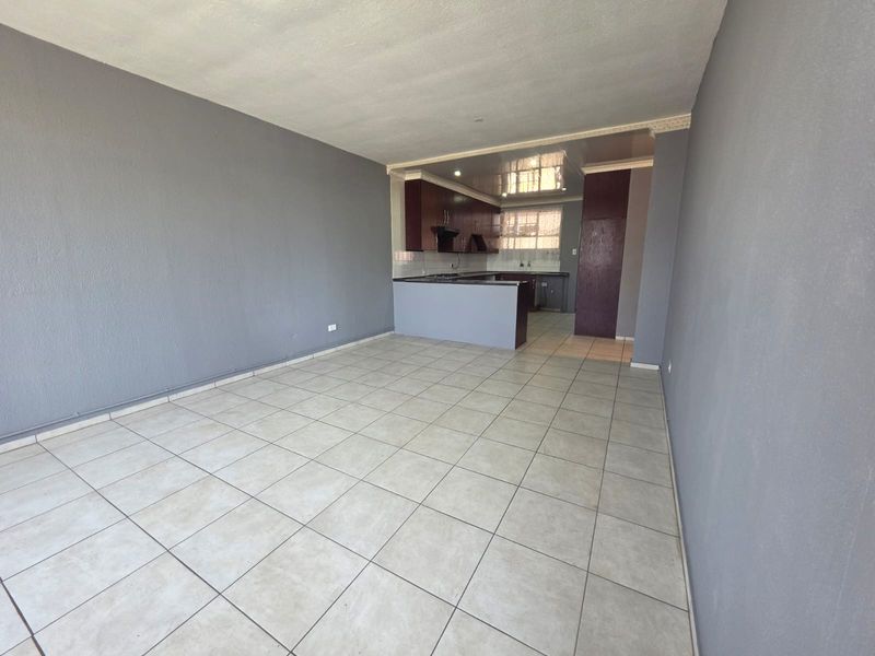 An open-plan living and kitchen area featuring neutral tiled flooring, grey walls, and dark wood-finish kitchen cabinetry with a functional peninsula layout.