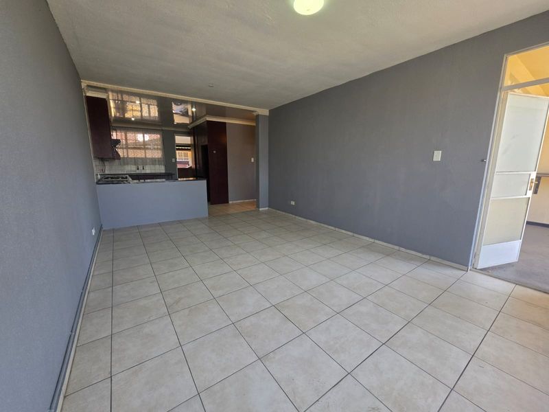 An open-plan living and kitchen area featuring neutral tiled flooring, grey walls, and a functional kitchen layout with built-in cabinetry.