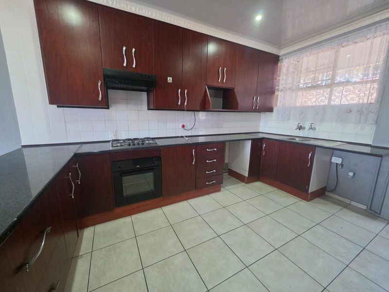 A functional kitchen featuring dark wood cabinetry, granite countertops, a gas hob, built-in oven, and tiled flooring with a clean, neutral backsplash.