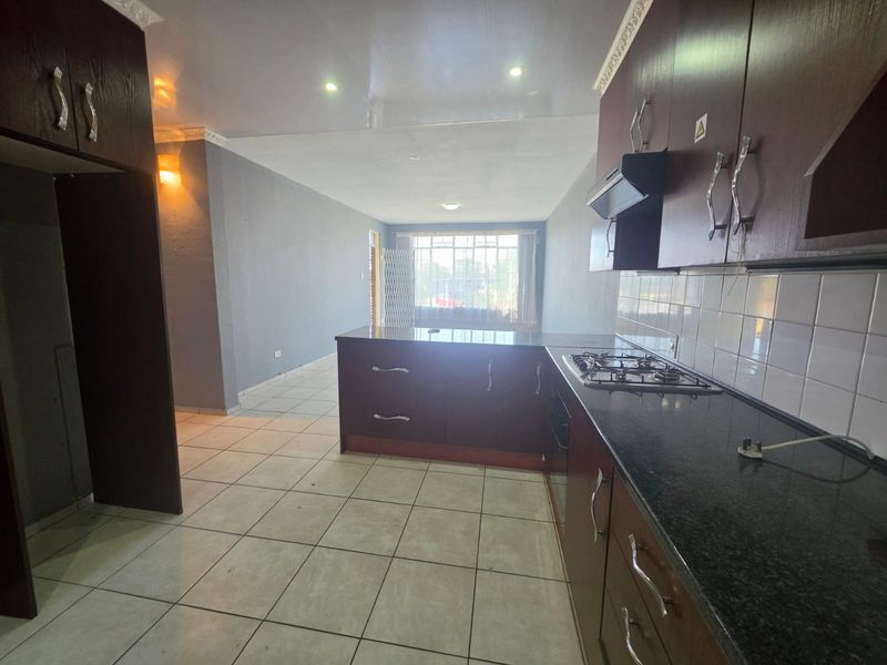 Open-plan kitchen and living area featuring dark wood cabinetry, granite countertops, gas hob, extractor fan, and tiled flooring throughout.
