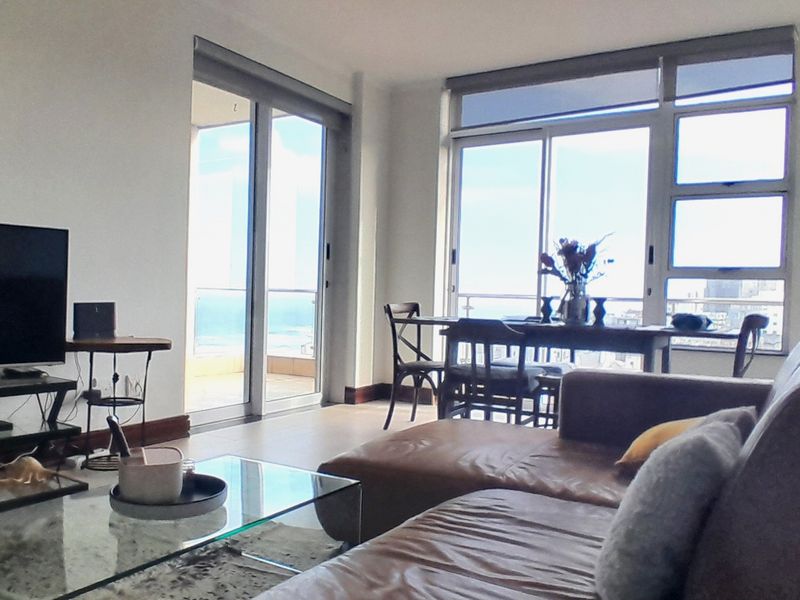 Bright open-plan living and dining area featuring large windows and sliding glass doors that provide ample natural light and access to the balcony.