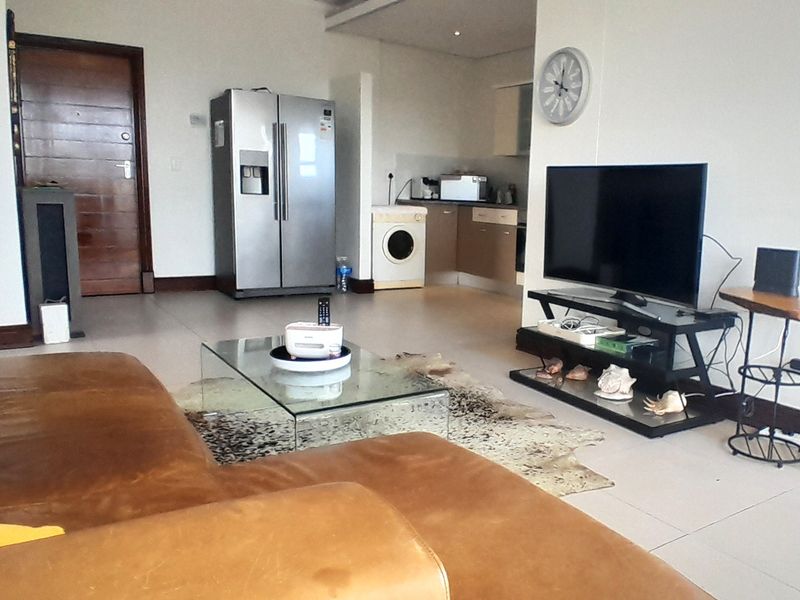 Open plan living area featuring tiled flooring and a compact kitchen with built-in cabinetry, seamlessly connecting the lounge and kitchen spaces.