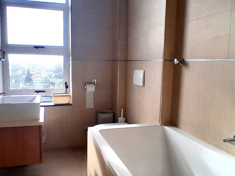 A functional bathroom featuring a wall-mounted vanity with basin, a bathtub, and neutral wall tiling, complemented by natural light from the window.