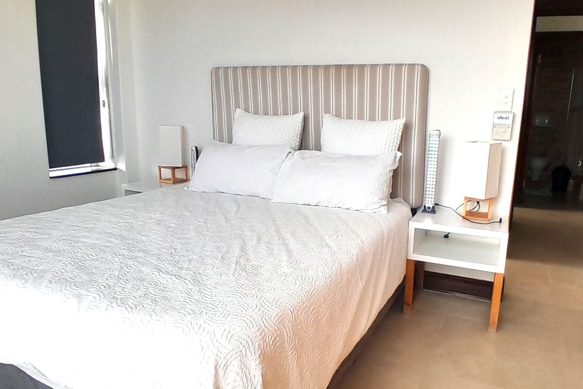 A well-lit bedroom featuring neutral tiled flooring, a roller blind, and direct access to an adjoining room.