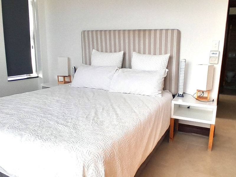 A well-lit bedroom featuring neutral tiled flooring, a roller blind, and direct access to an adjoining room.