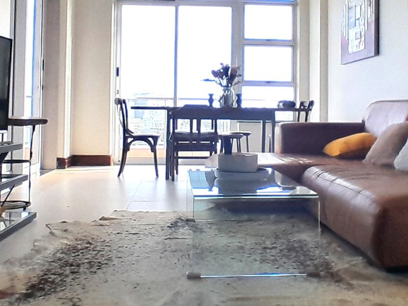 A bright living room featuring tiled flooring and large sliding glass doors that provide access to the balcony and natural light.