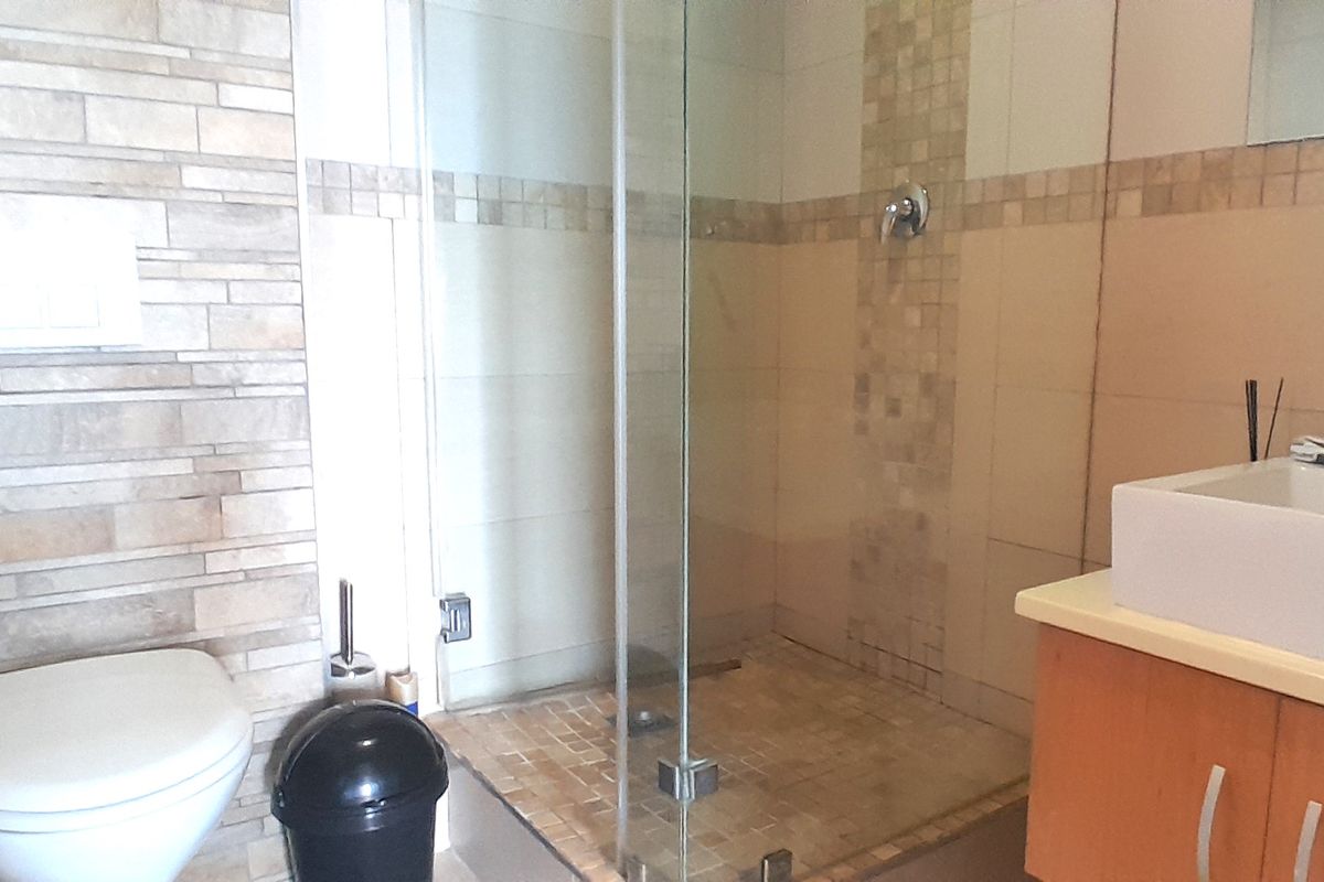Modern bathroom featuring a glass-enclosed shower, wall-mounted toilet, and a vanity unit with a basin, accented by decorative mosaic tiling.