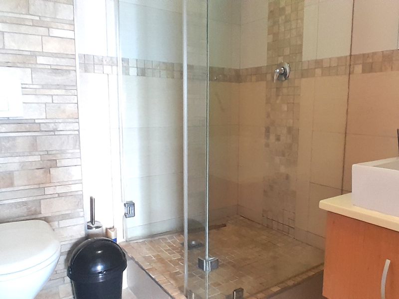 Modern bathroom featuring a glass-enclosed shower, wall-mounted toilet, and a vanity unit with a basin, accented by decorative mosaic tiling.
