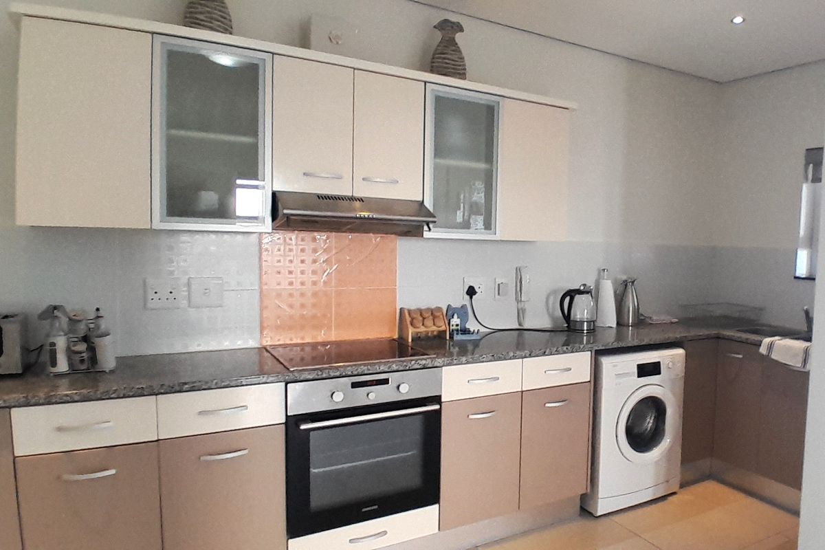 A functional kitchen featuring two-tone cabinetry, granite countertops, a built-in oven with hob, extractor fan, and an integrated washing machine.