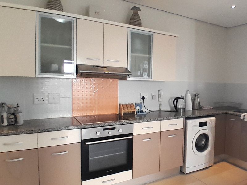 A functional kitchen featuring two-tone cabinetry, granite countertops, a built-in oven with hob, extractor fan, and an integrated washing machine.